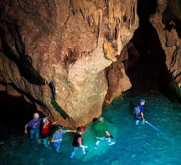 Guided group wading through turquoise water inside the cathedral-like ATM cave