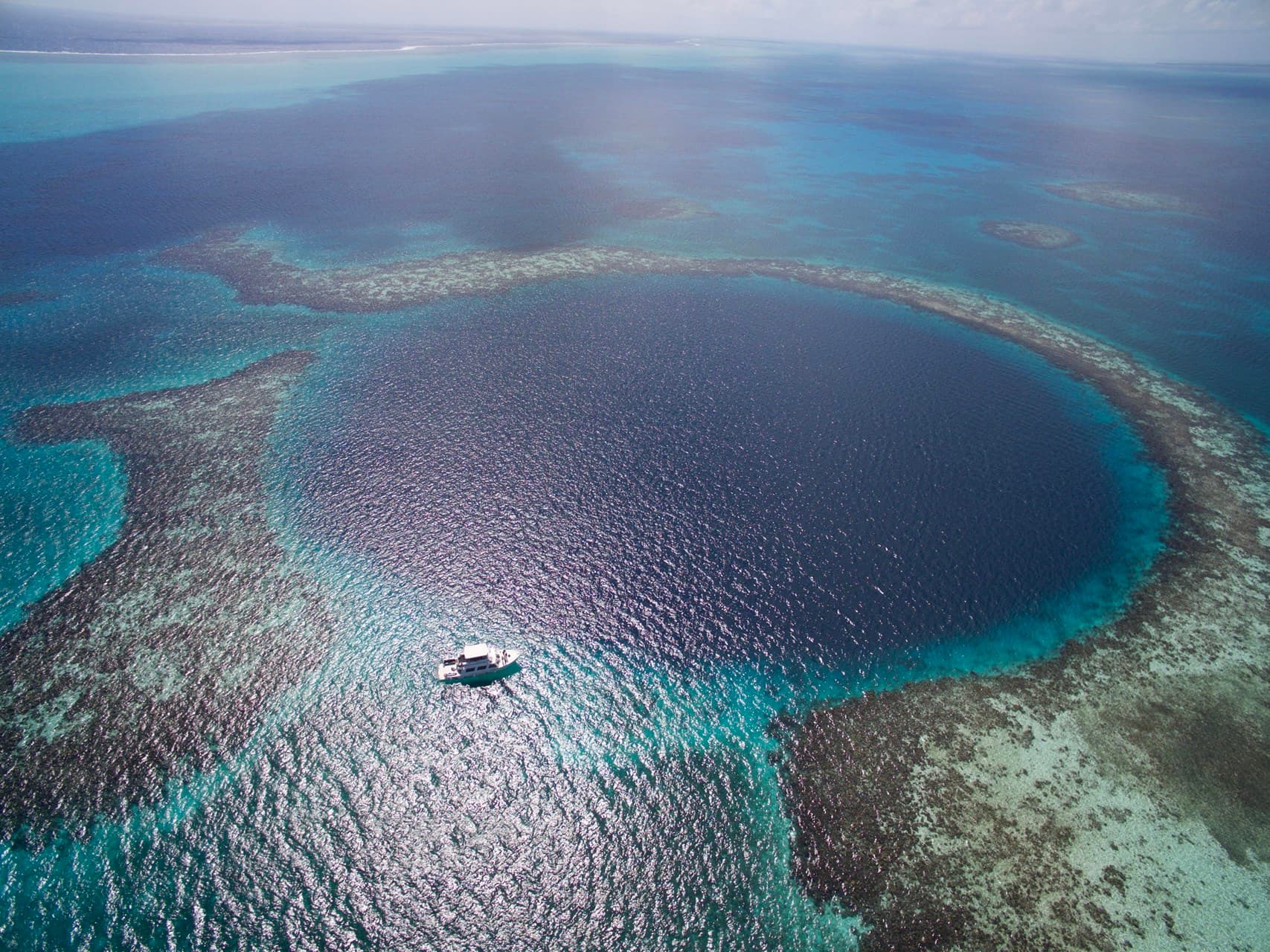 Aerial view of the Great Blue Hole, a deep circular sinkhole ringed by turquoise reef with a boat at its edge