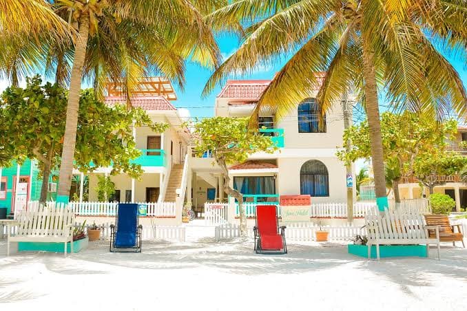 Teal and white beachfront guesthouse with colourful deck chairs on the sand under palms, Caye Caulker