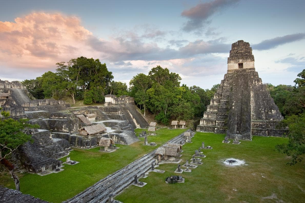 Ancient Maya stone temples and plaza rising above the rainforest at dusk
