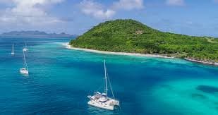 Yacht sailing past the green headlands of Grenada's sheltered south coast under a clear sky