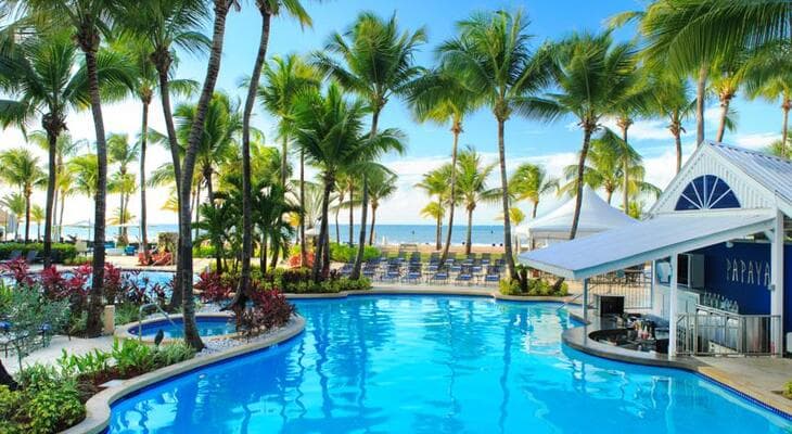 A palm-fringed resort pool with a thatched bar leading to the beach in Isla Verde, San Juan