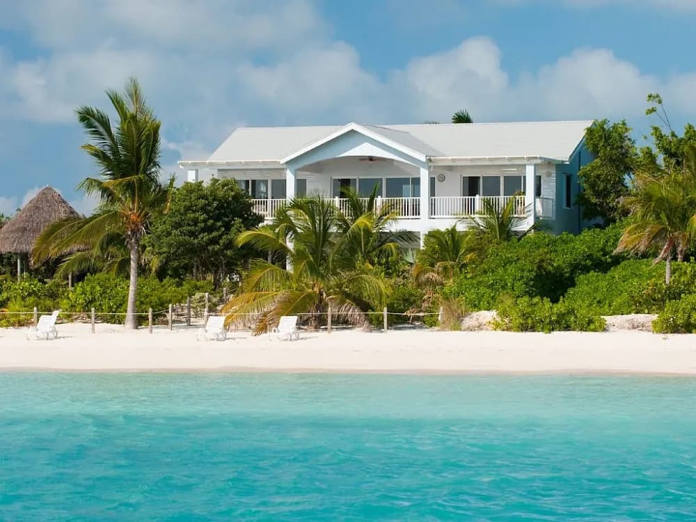 White beachfront villa among palms, facing the calm shallow water of Sapodilla Bay