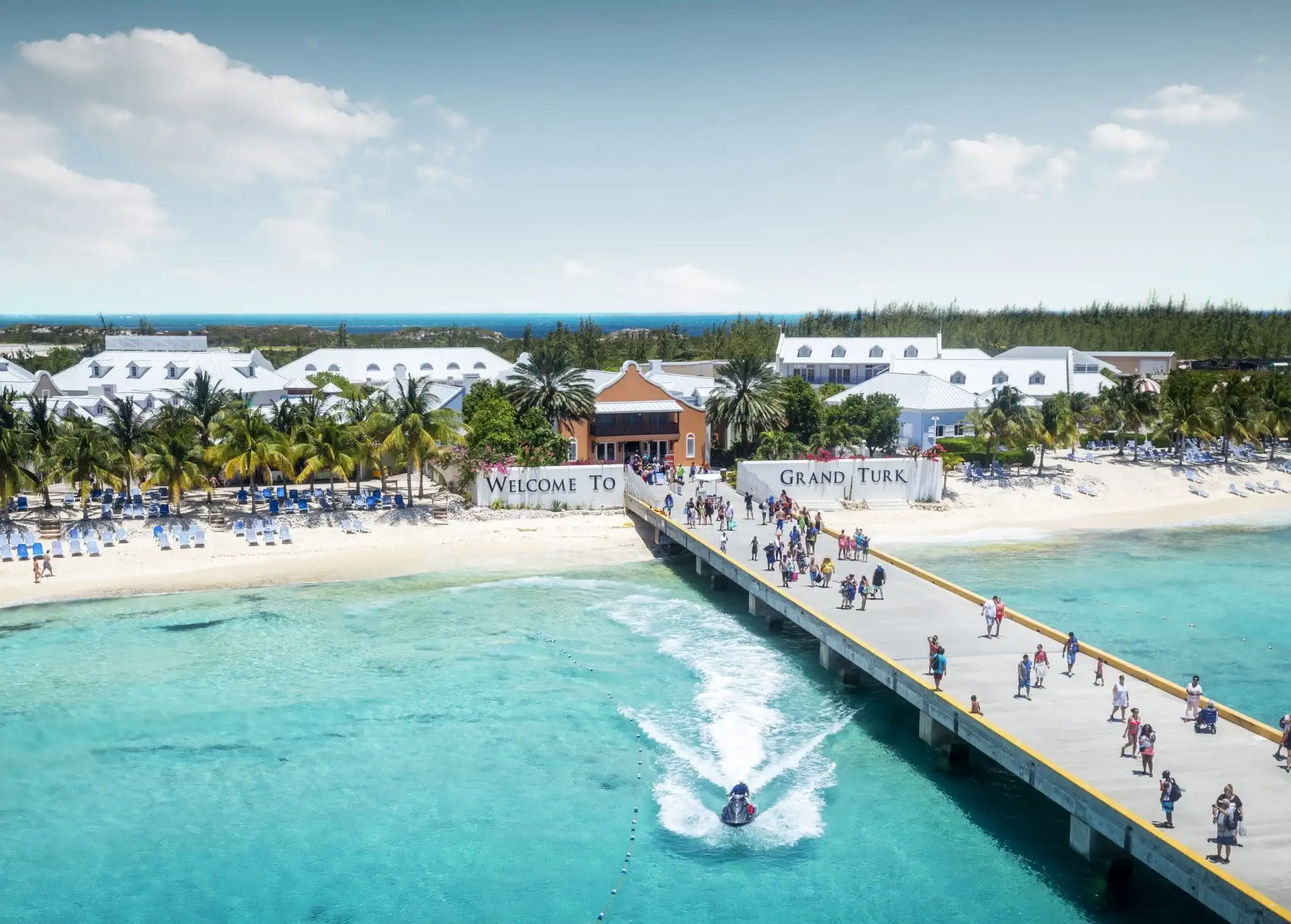 Cruise passengers walking the Grand Turk pier past the Welcome to Grand Turk sign beside Cruise Center Beach
