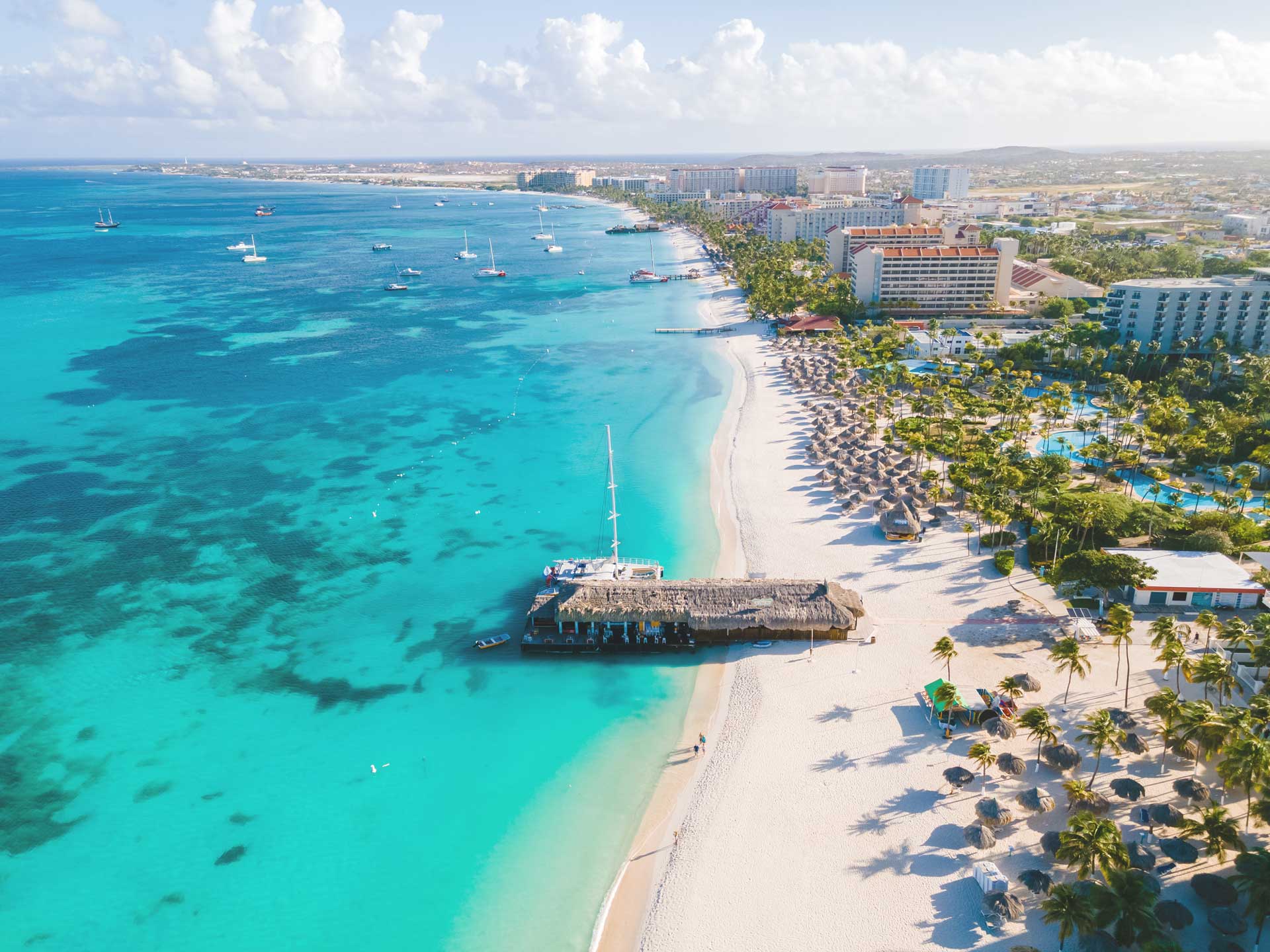 Aerial view of Palm Beach, Aruba, turquoise water, white sand, palapas and the resort strip
