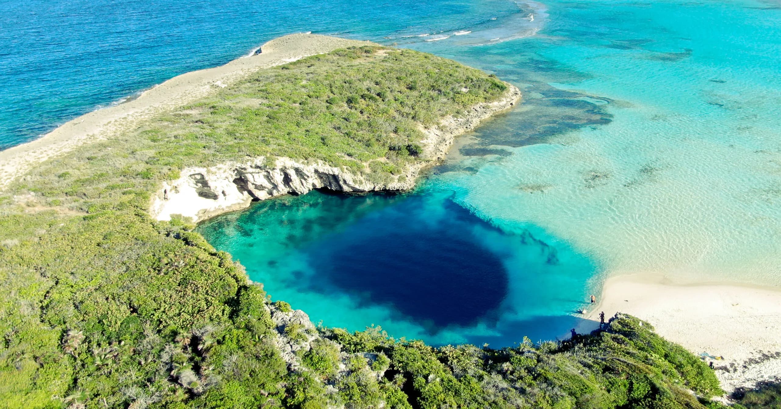 An aerial view of the perfectly circular deep blue Dean's Blue Hole surrounded by white cliffs and turquoise water on Long Island, Bahamas