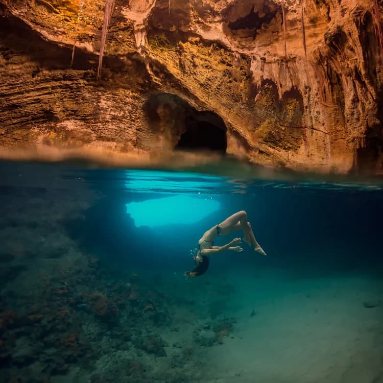 Snorkellers exploring the dramatic sea cave opening of Thunderball Grotto surrounded by fish in Staniel Cay, Exuma