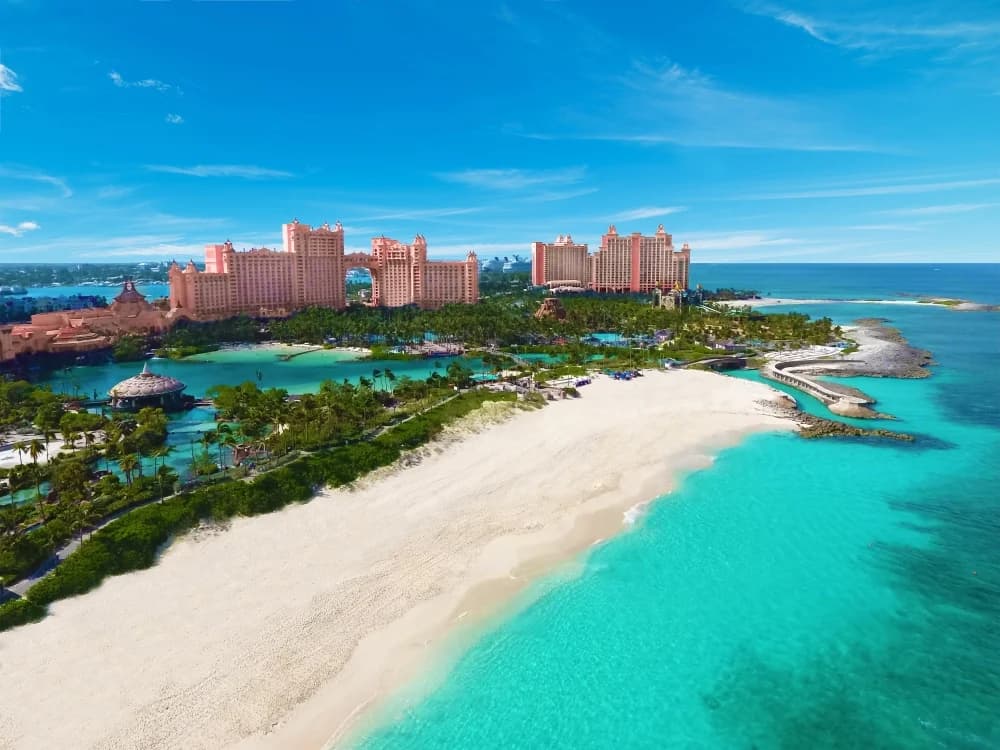 Aerial view of luxury resort pools and a white sand beach fronting the calm blue water of Nassau, New Providence, Bahamas