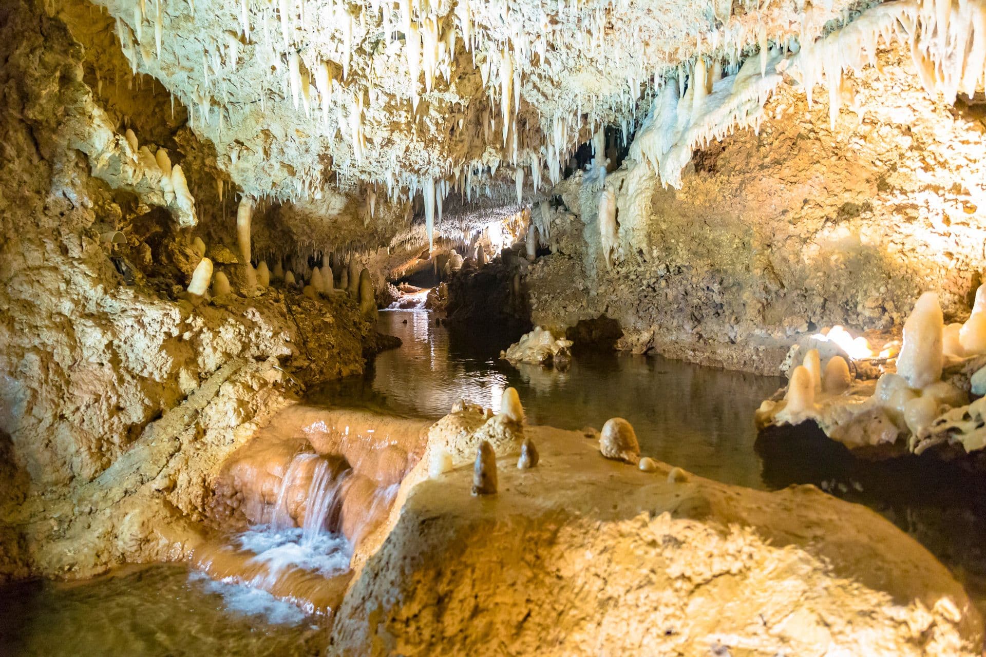 Illuminated stalactites, stalagmites and a flowing stream inside Harrison's Cave in Barbados