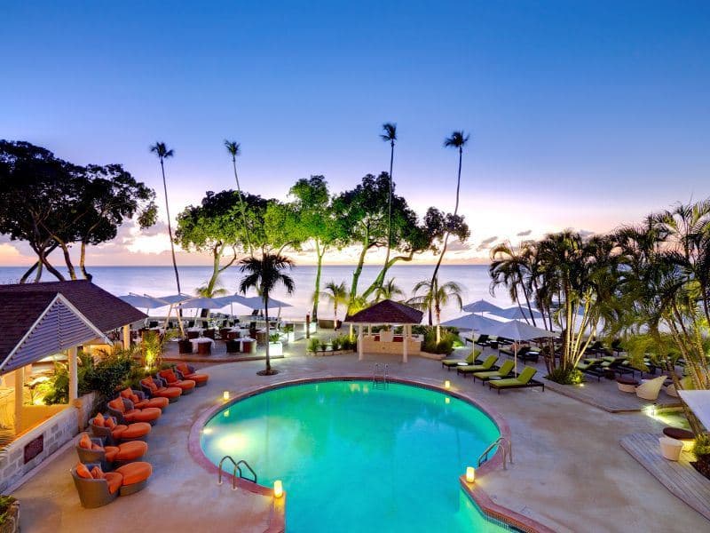 Palm trees and loungers around a lit poolside terrace at a luxury west coast resort in Barbados at sunset