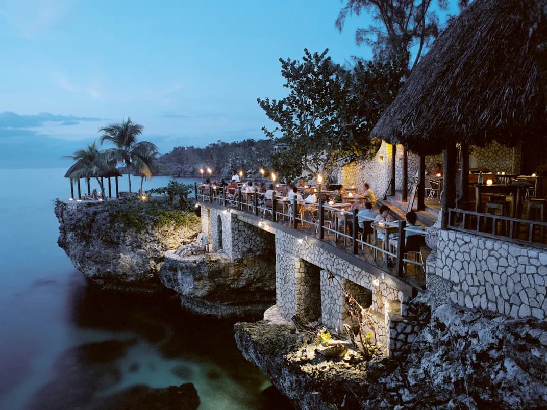 Diners at a candlelit cliff-top restaurant overlooking the sea at dusk in Negril, Jamaica