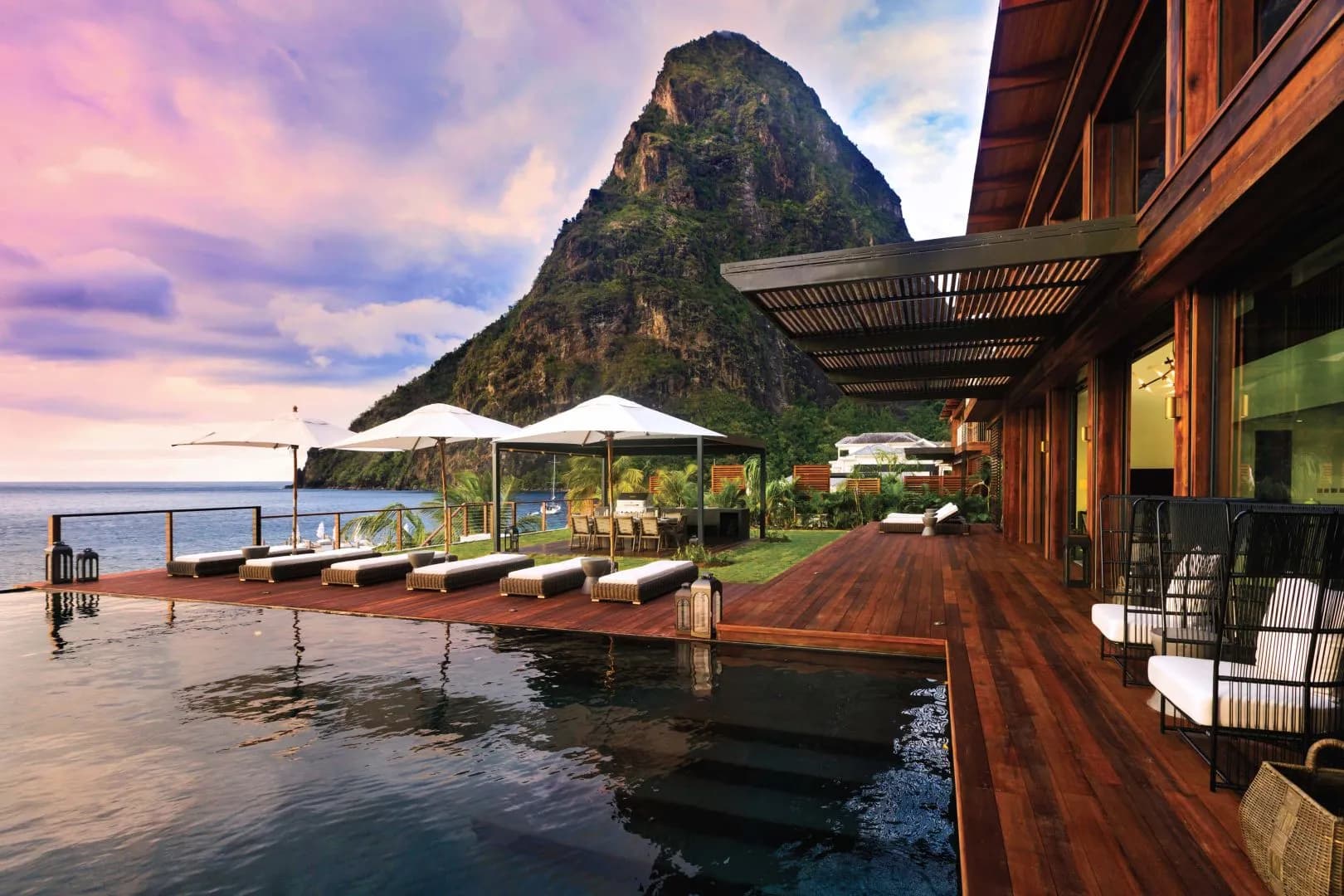 Infinity pool and sun loungers on a luxury resort deck with Petit Piton rising from the Caribbean Sea at sunset, Saint Lucia