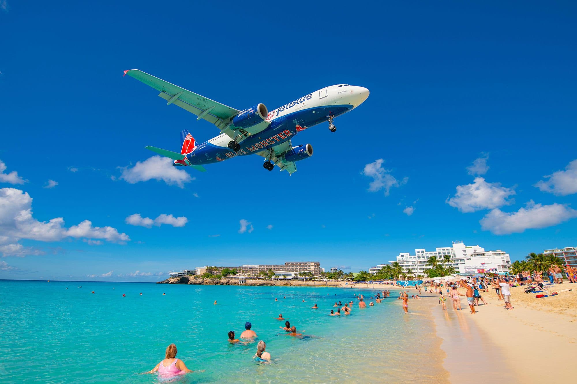 A jet landing low over Maho Beach beside turquoise water in Sint Maarten