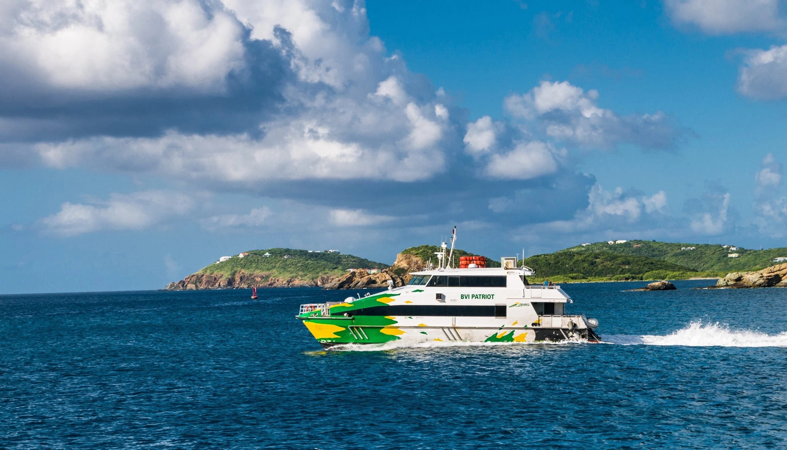 The green and yellow BVI Patriot passenger ferry crossing blue water toward the British Virgin Islands