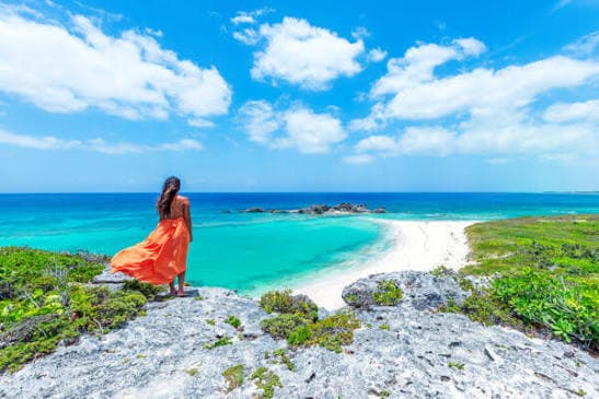 Woman in an orange dress overlooking a quiet curved beach and turquoise sea on North Caicos